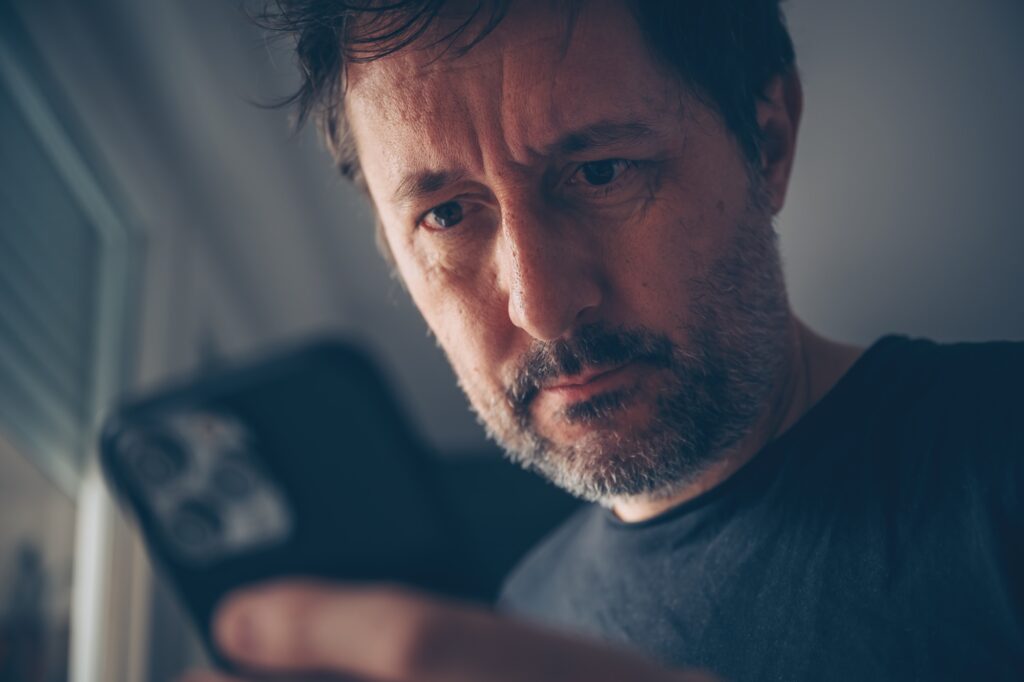 Surprised man looking at mobile phone text message recognizing sms scam and fraud activity